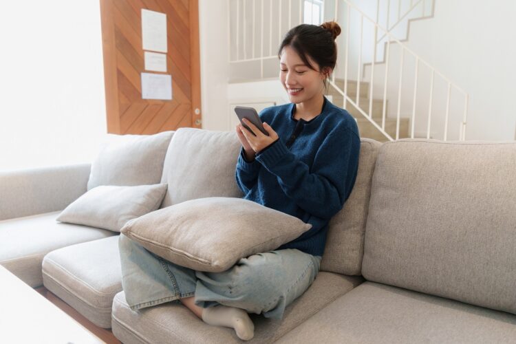 happy young asian woman using smartphone sitting on couch. 