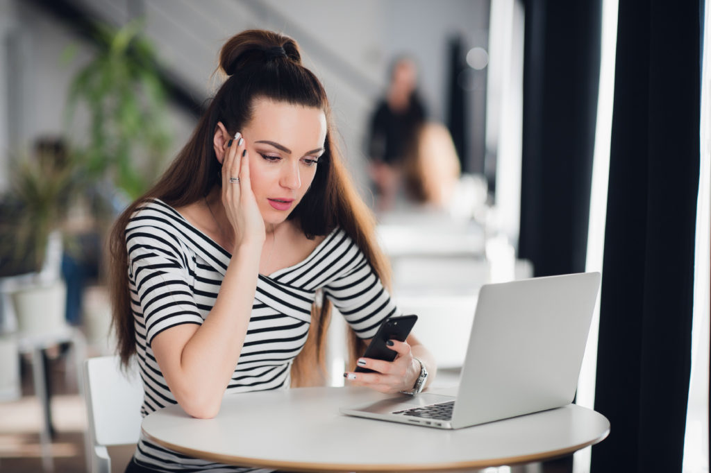 Shocked woman holding and looking sadly at mobile phone.