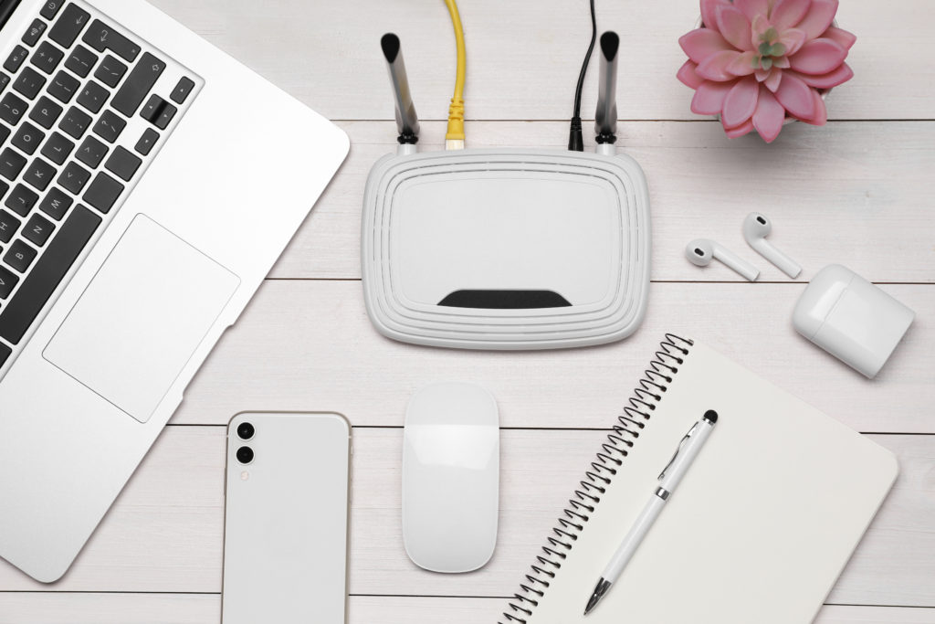 Router, smartphone, laptop and office stationery on white wooden table.