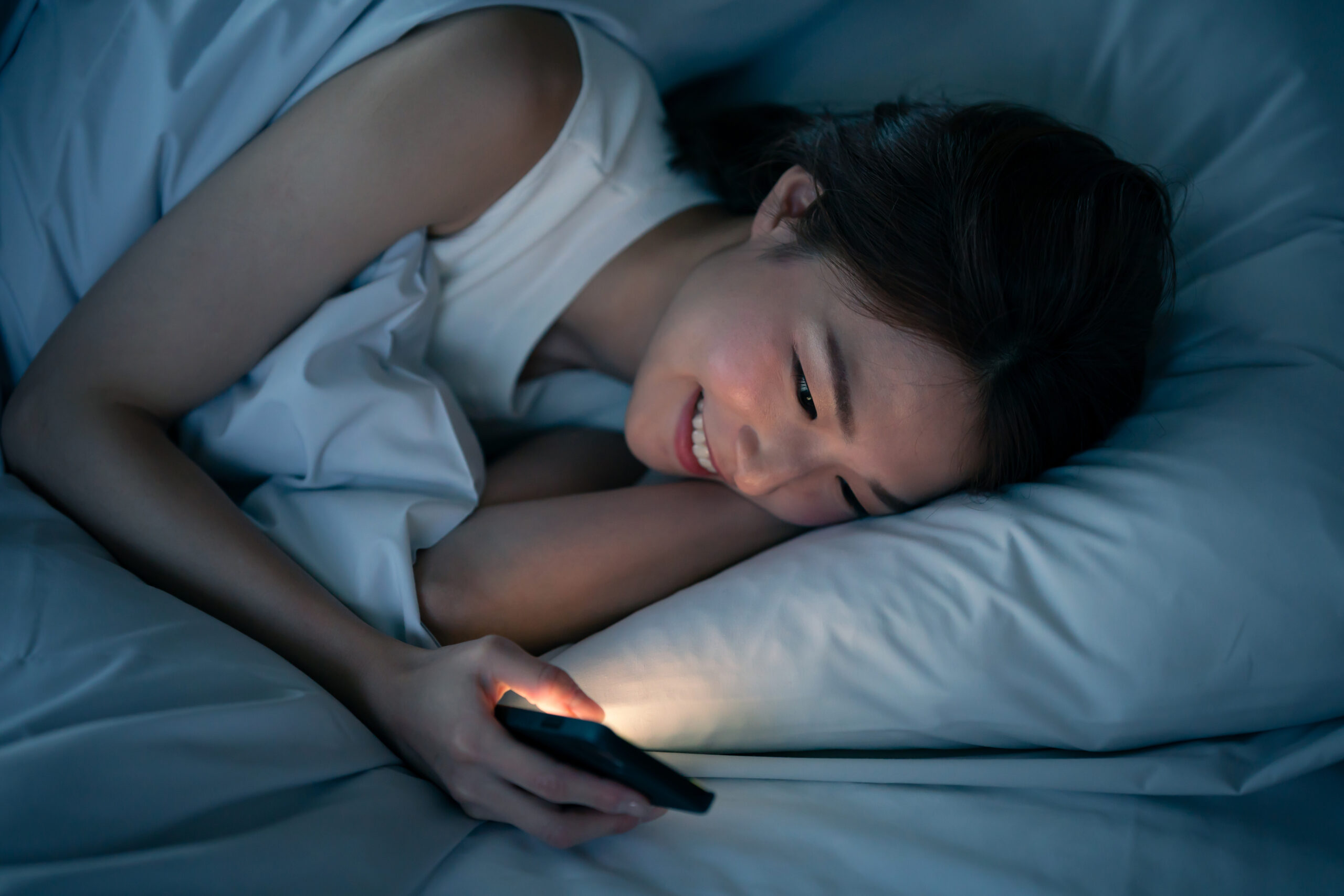 woman using phone laying in bed at night