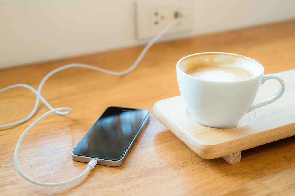 phone charging, plugged on the wall, and a cup of latte.