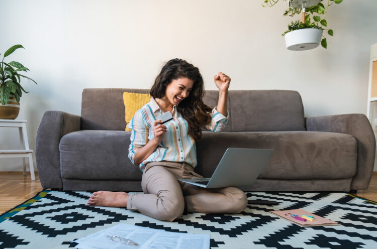 Excited woman holding credit card and using laptop computer.