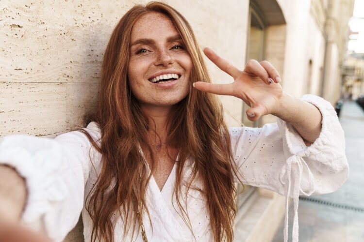Attractive redhead with freckles gesturing peace sign and taking selfie