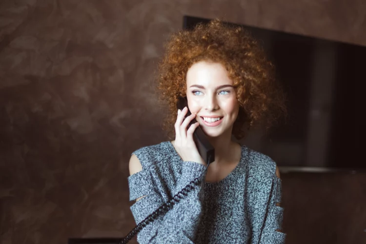Beautiful happy woman talking on landline telephone in the room