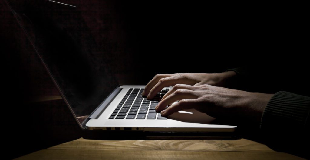 Man typing on laptop in a dark room.