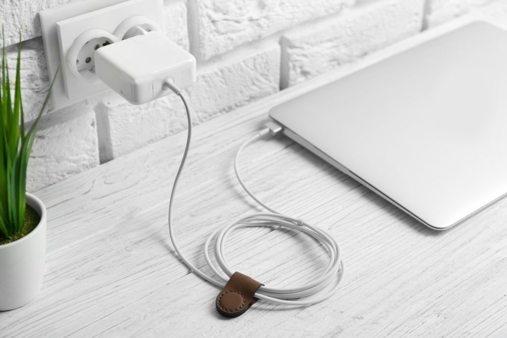 Laptop plugged into wall charger with cable organizer.