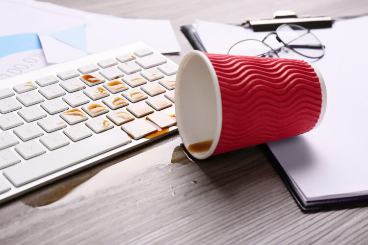 Cup of coffee spilled over computer keyboard on wooden office desk