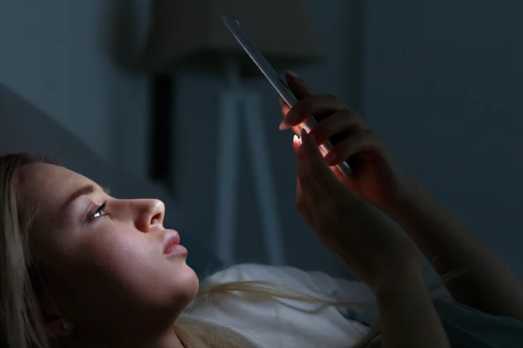 young woman using phone while lying in the bed at night