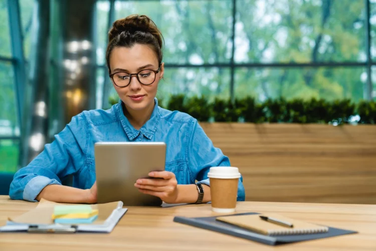 Nice-looking young woman using tablet at the desk in modern office