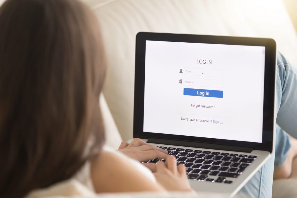 Woman opening login page on her laptop while sitting on sofa.