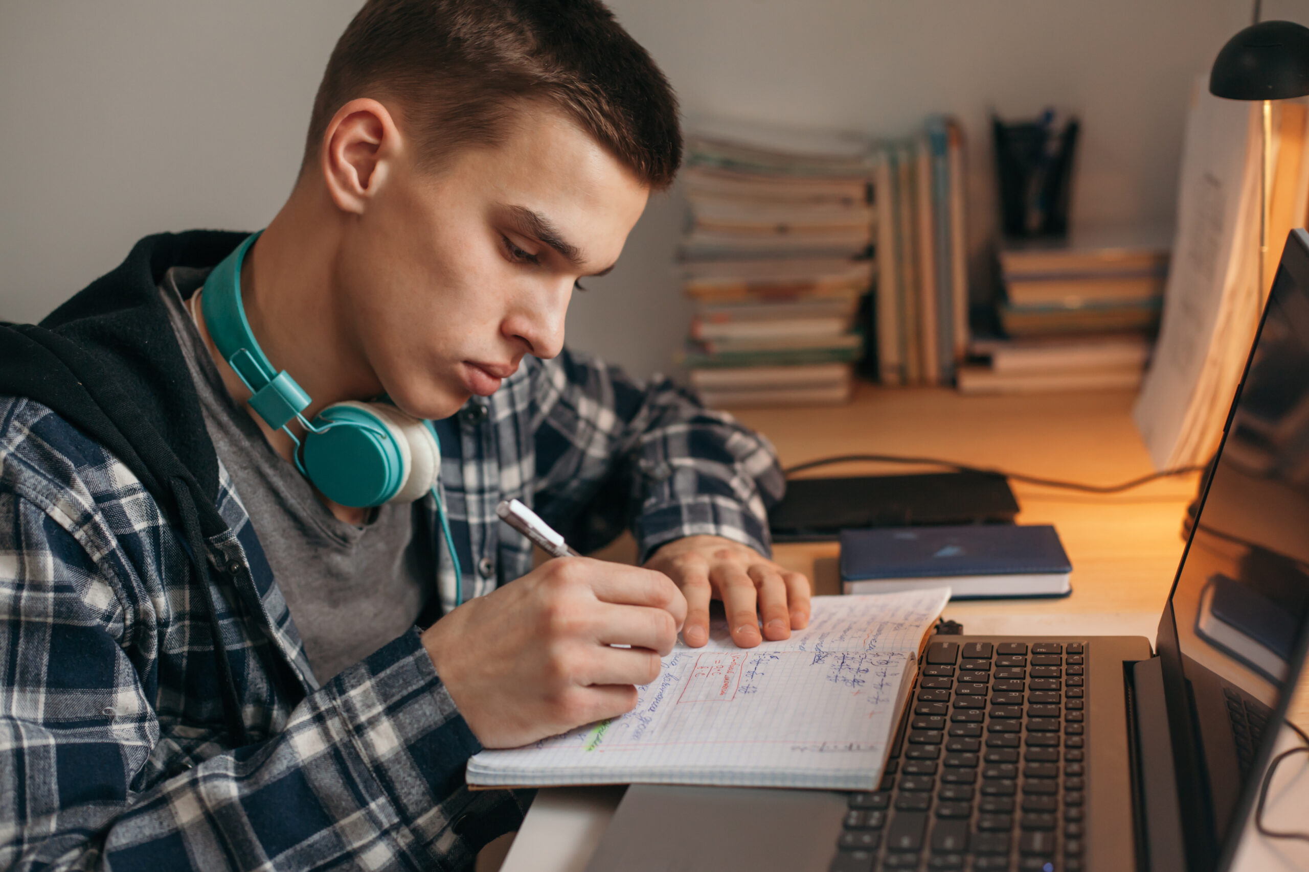 Teenage boy doing homework using computer sitting by desk in roo