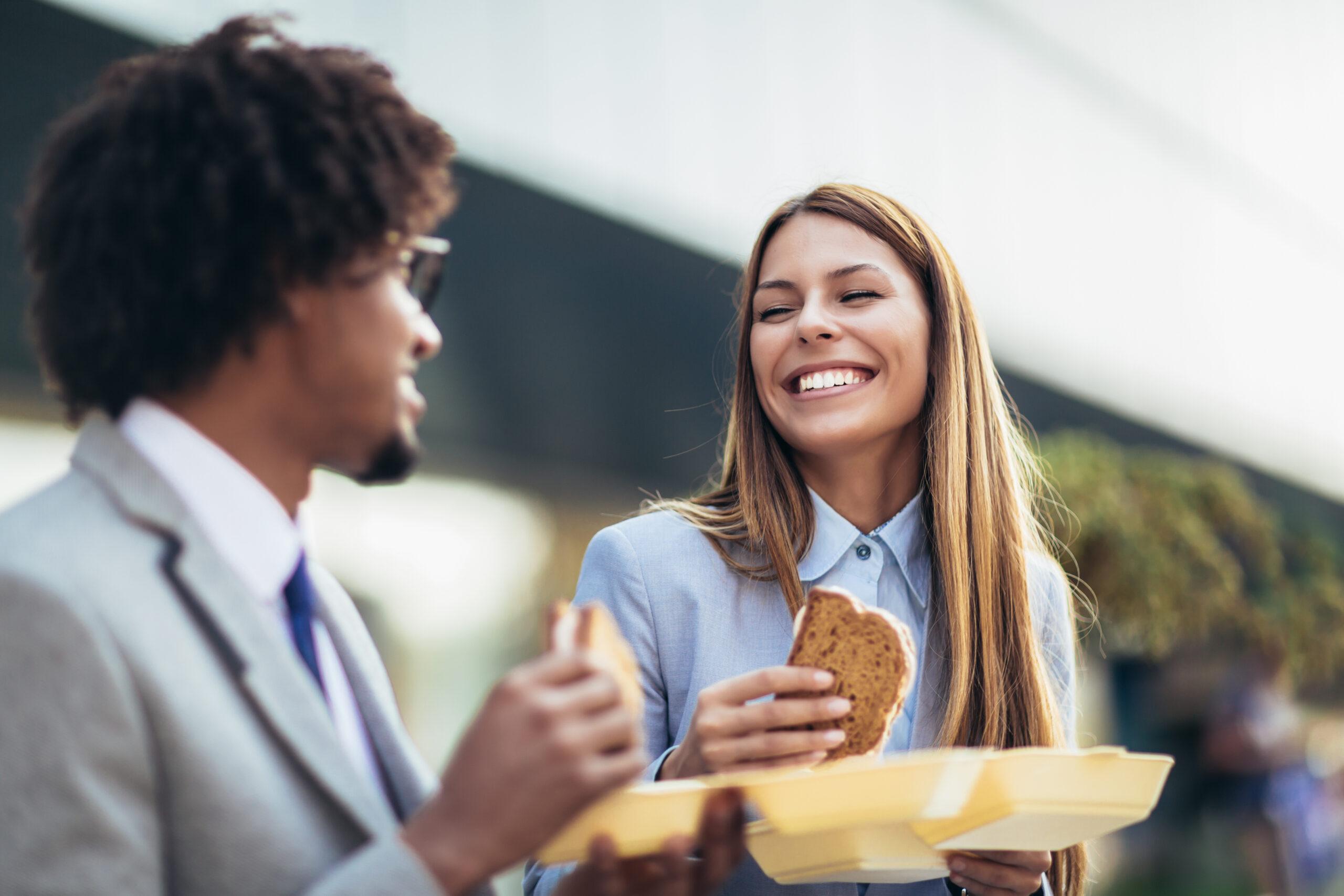 Smiling businessmen with sandwiches sitting in front of the offi