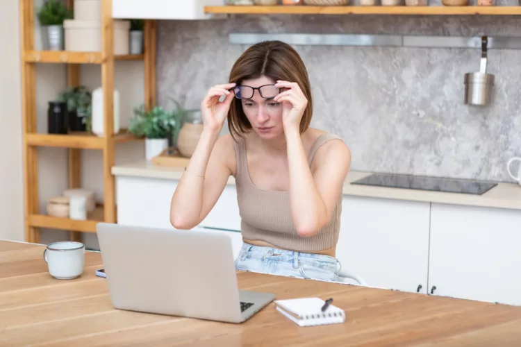 woman looking at laptop lifting her glasses off