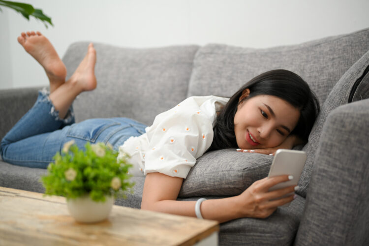 Relaxed woman lying on comfortable sofa and enjoy on her smartphone.