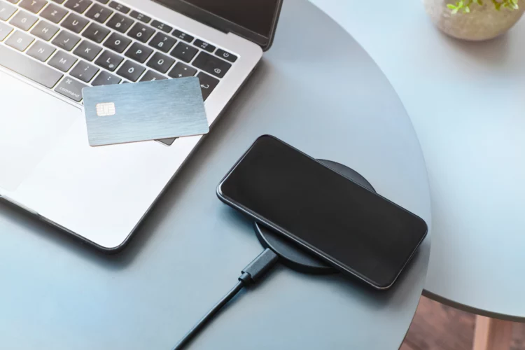 Using wireless charger to recharge smartphone battery next to laptop.