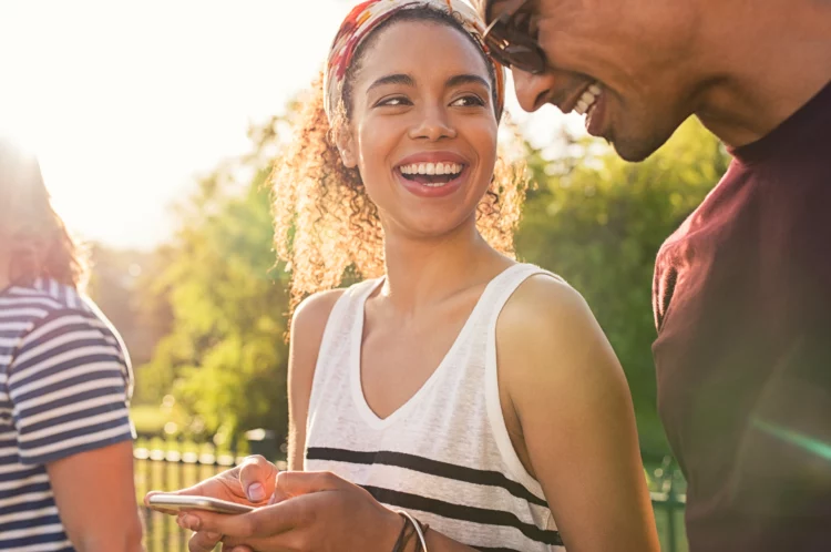 man and woman smiling outdoor with smartphone in hand