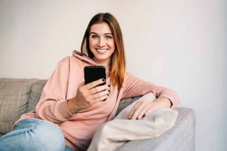 Happy woman using mobile phone on sofa
