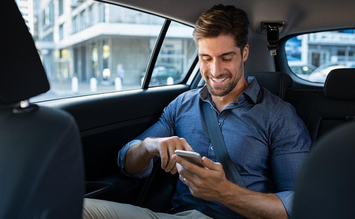 Hombre sonriente feliz usando el teléfono mientras está sentado en un taxi 