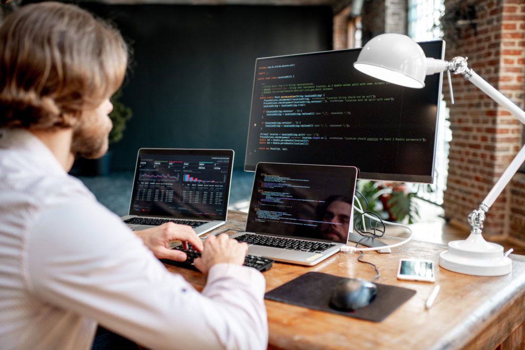 Male programmer in his workplace with three monitors.