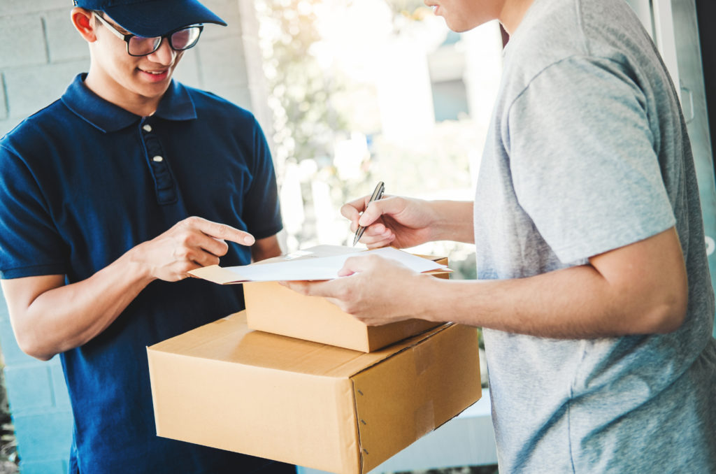 Man receives package and signs the document on the clipboard.