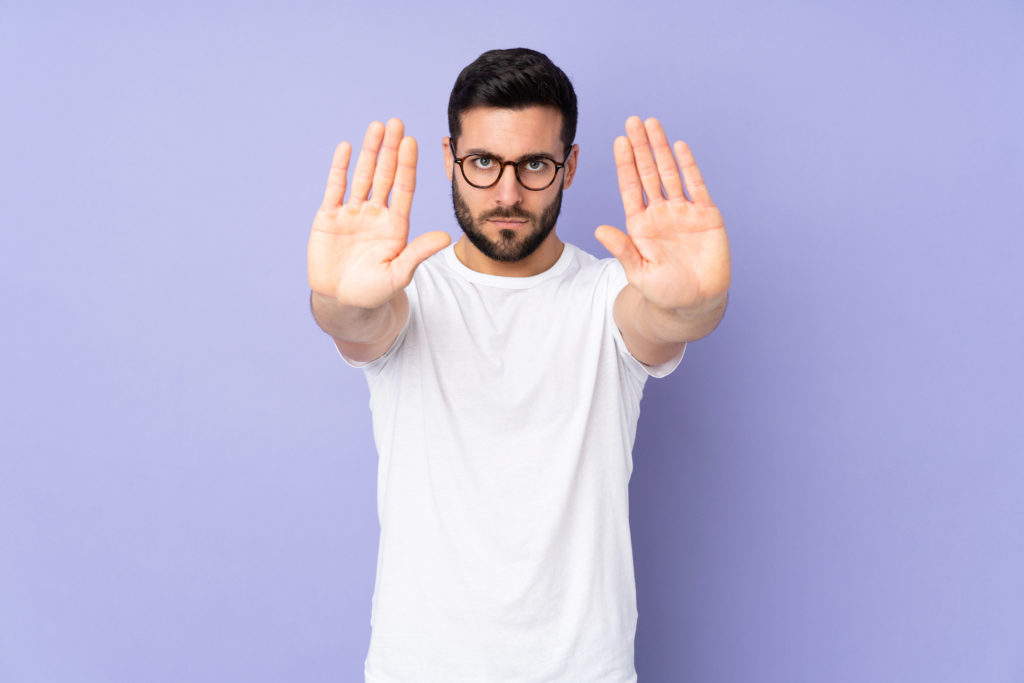 Man doing a 'stop' sign with his hands, blue background.