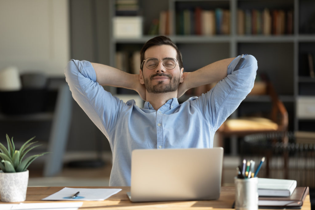 Man takes a break from his work and laptop, leans back on chair.