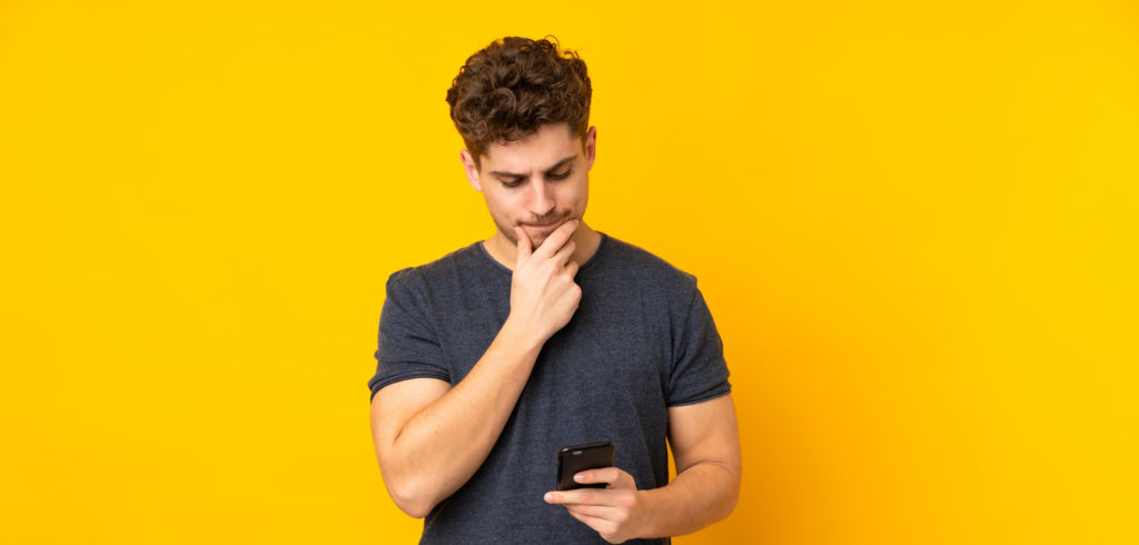 Man thinking while looking at his phone, yellow background.