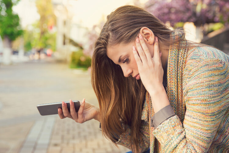 Upset woman with smartphone on street