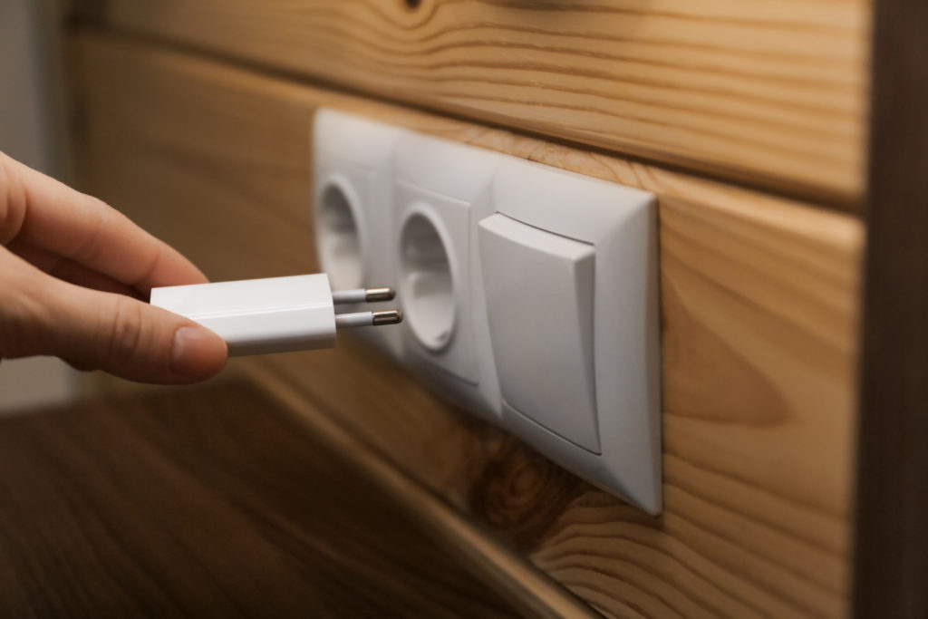 Woman putting charging plug with USB cable into socket on wall