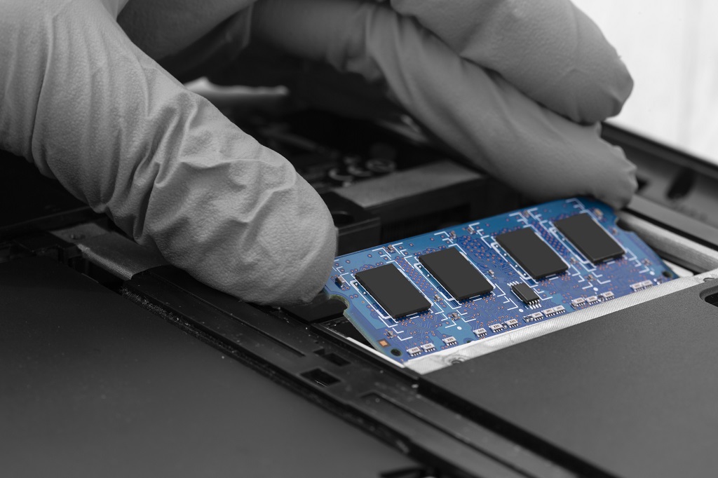 Technician installing RAM into the memory slot on a laptop computer.