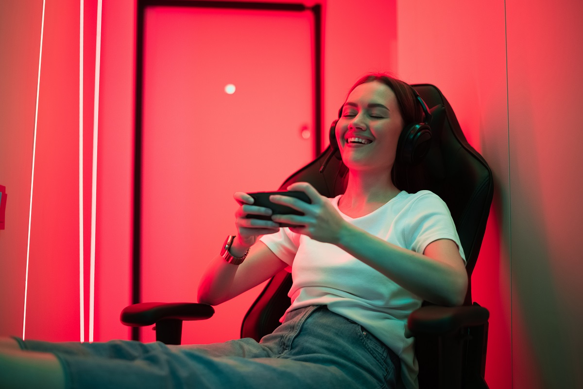 satisfied young lady sitting on gaming chair with cellphone in hands