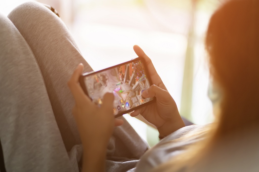 Girl is playing a mobile game with blurred on screen in living room.
