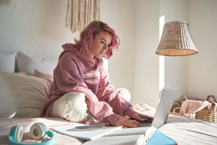 Hipster teen student with pink hair using laptop.