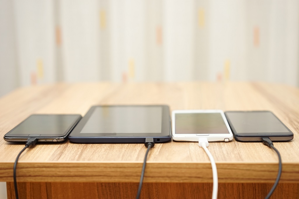 Computer tablet and mobile phones charging on home desk.