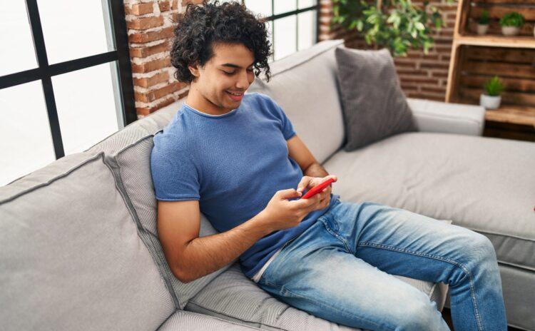 Young Hispanic man using smartphone sitting on sofa at home