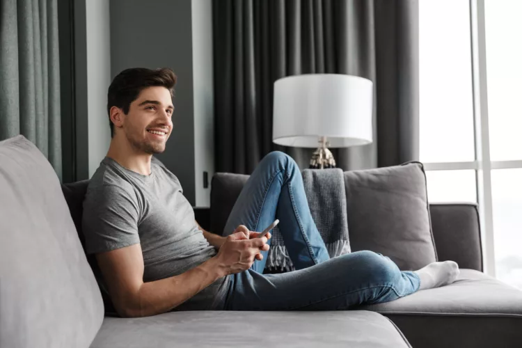 Attractive young bearded man sitting on a couch while using his smartphone