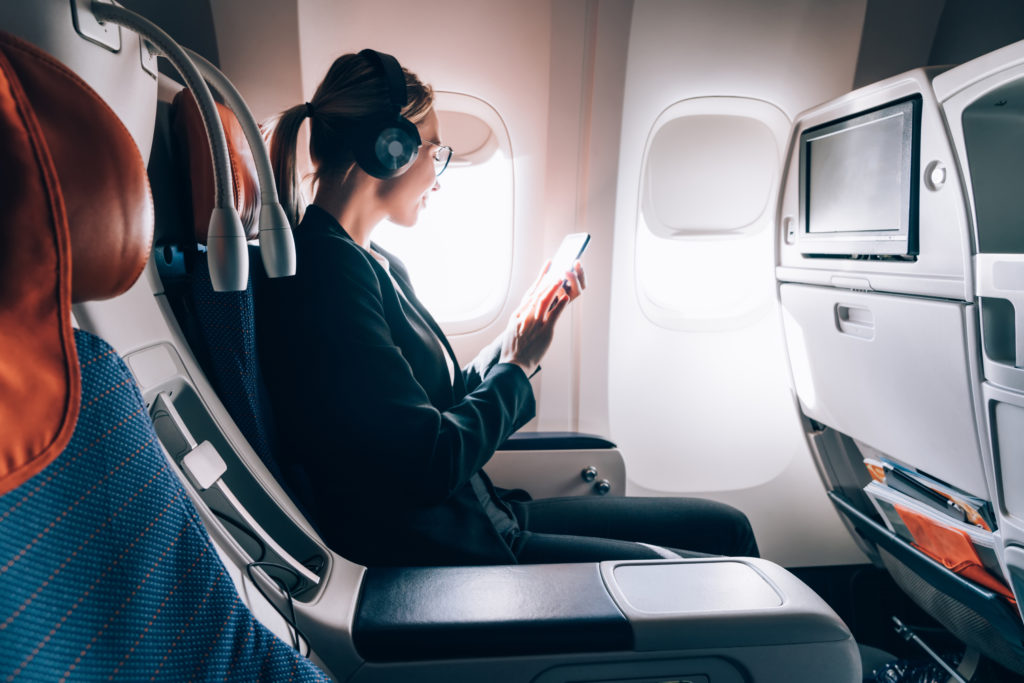Female airplane passenger seated in her designated seat, reading messages on her phone.