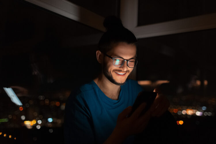 devious looking smiling man looking in smartphone in dark room at night