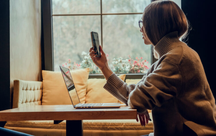 Young beautiful woman using smartphone in a coffee shop to notify contacts of new phone number.