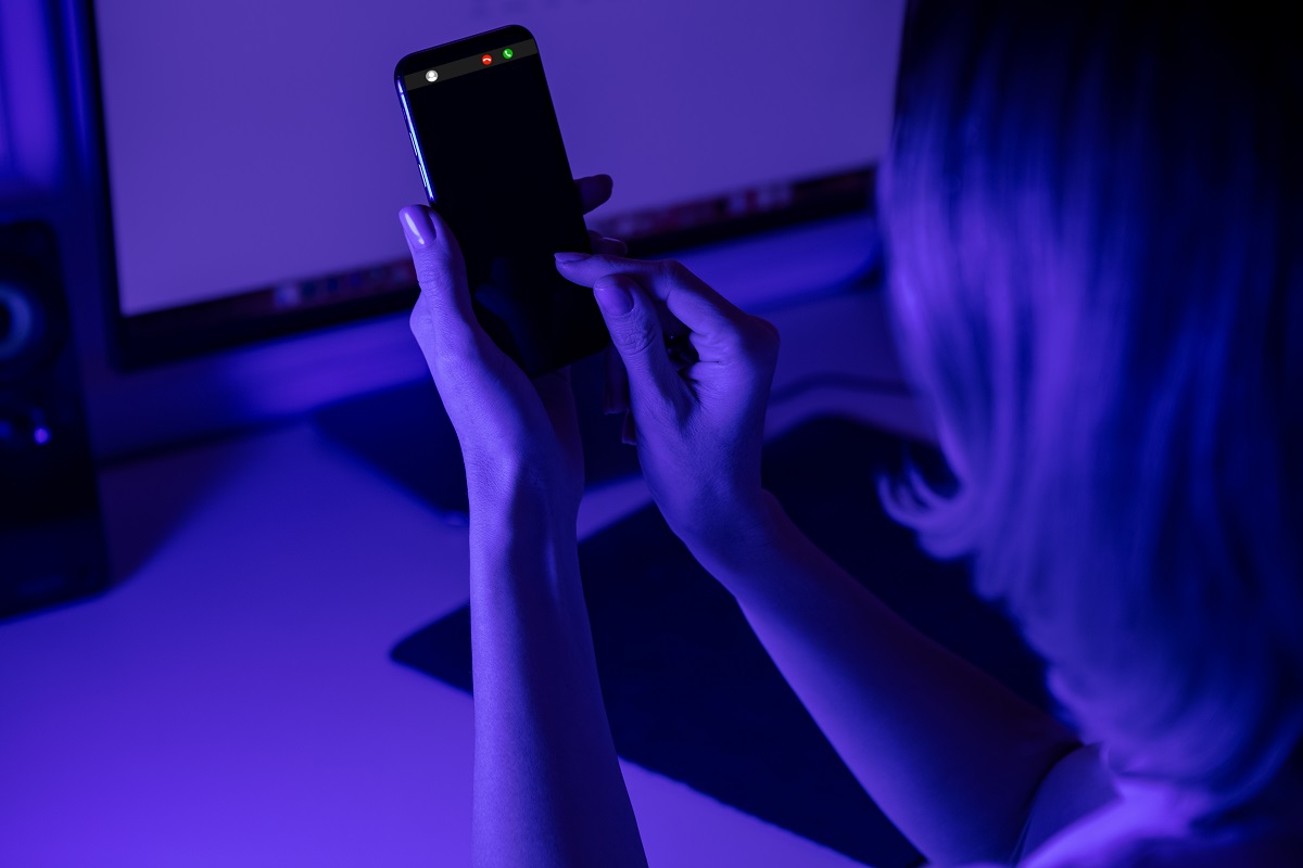 Silhouette of a person holding mobile phone in hand, in dimly lit room