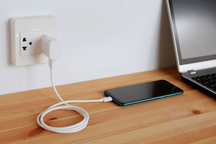 Adapter cord charger of smart phone on wood desk, plugged in power outlet.