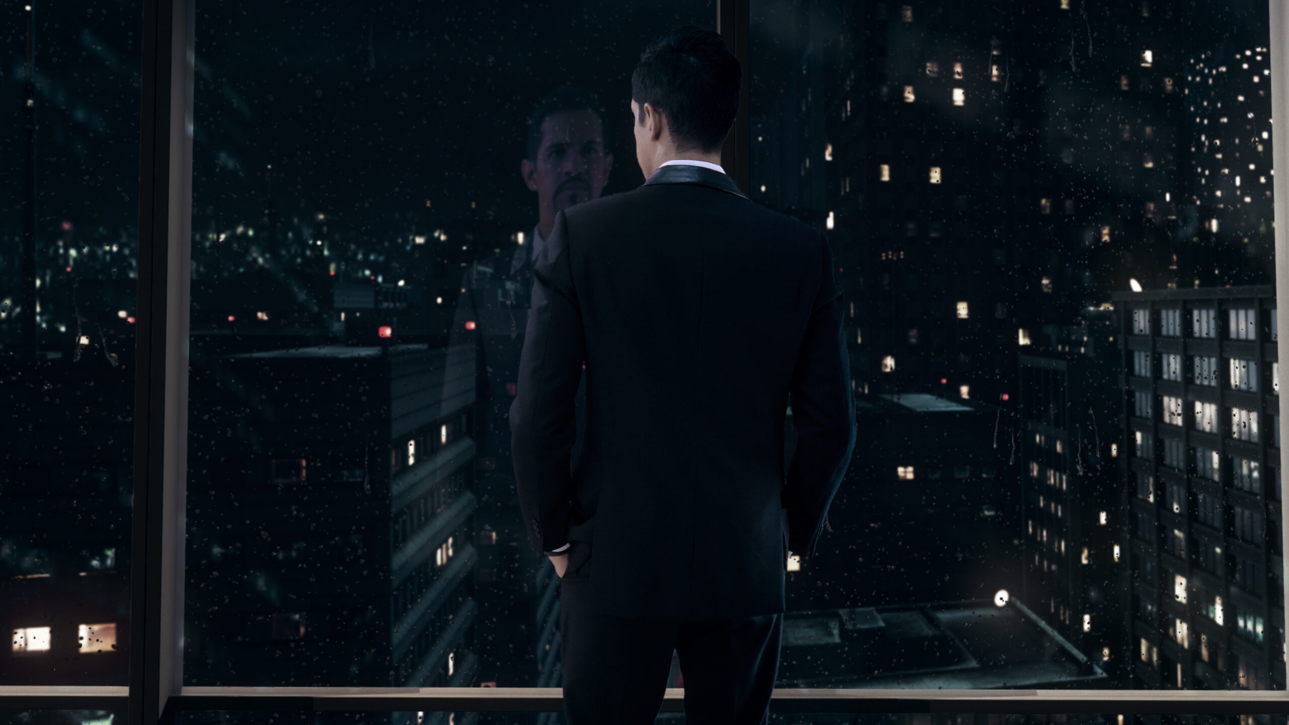 Man in black suit standing by the window to look out into the dark city