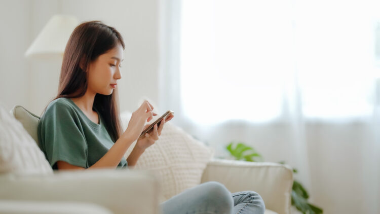 Happy young woman relax on comfortable couch at home using her smartphone.