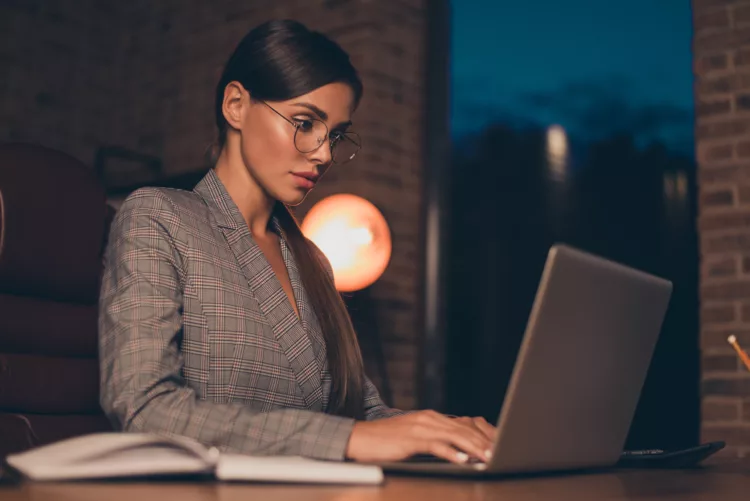 Woman with glasses intently typing on her laptop late in the evening
