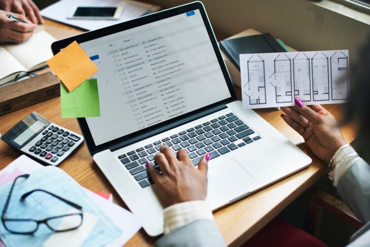 Left hand of a woman on the keyboard while other hand holds project designs