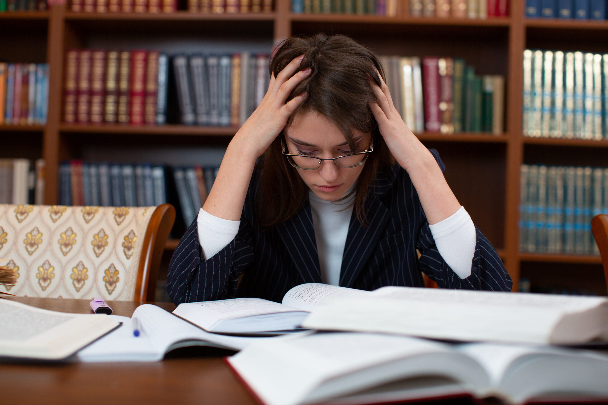 young woman holds her head in disappointment at desk with open books