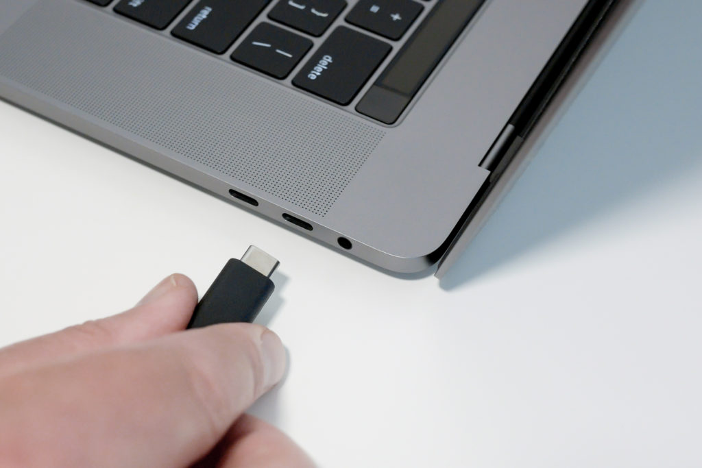 Man's hand plugging in black USB Type C cable into USB-C port on laptop.