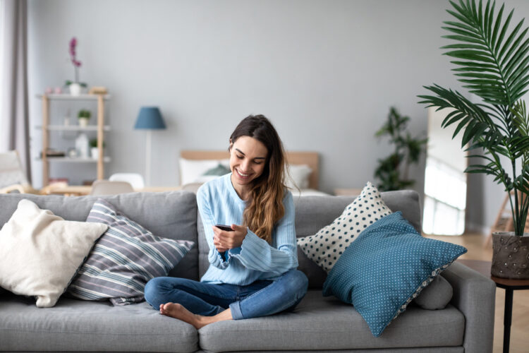 Smiling woman online chatting on her phone at home.