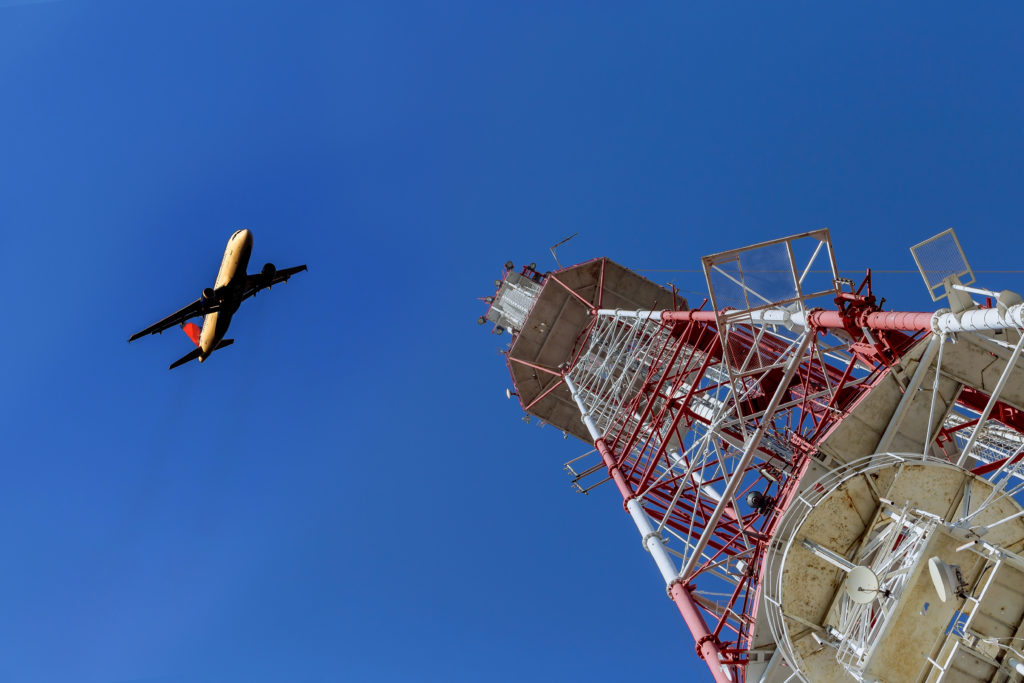Telecommunications tower against blue sky with an airplane just taken off.