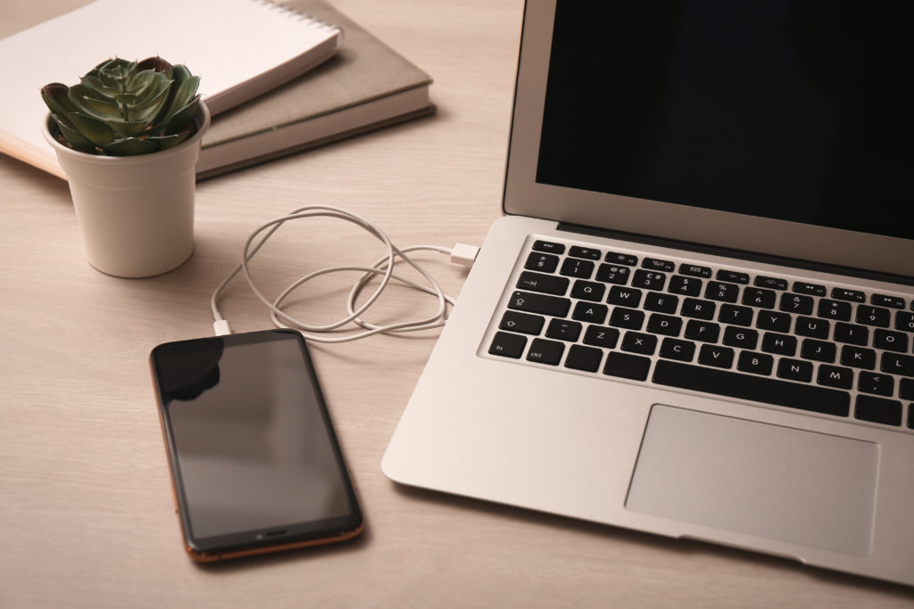 Smartphone connected with charge cable to laptop on wooden table